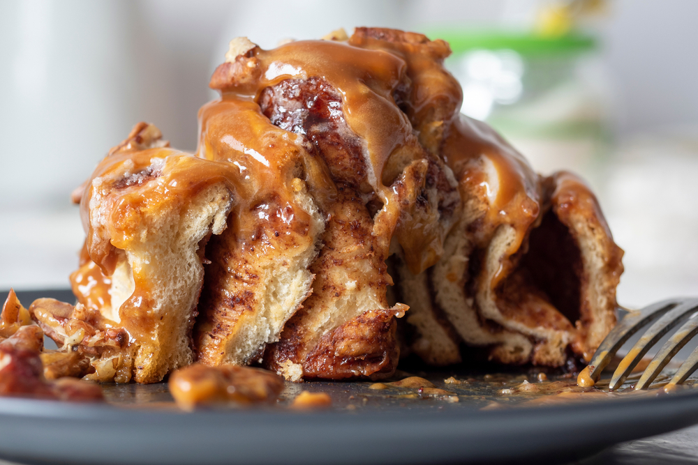 cinnamon,bun,drizzled,with,topping,and,garnished,with,pecans.,cut