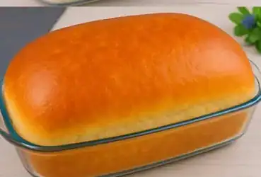 Pão caseiro de 1kg grande, macio e dourado, recém-assado em forma sobre superfície rústica