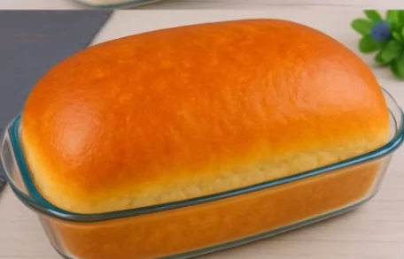 Pão caseiro de 1kg grande, macio e dourado, recém-assado em forma sobre superfície rústica